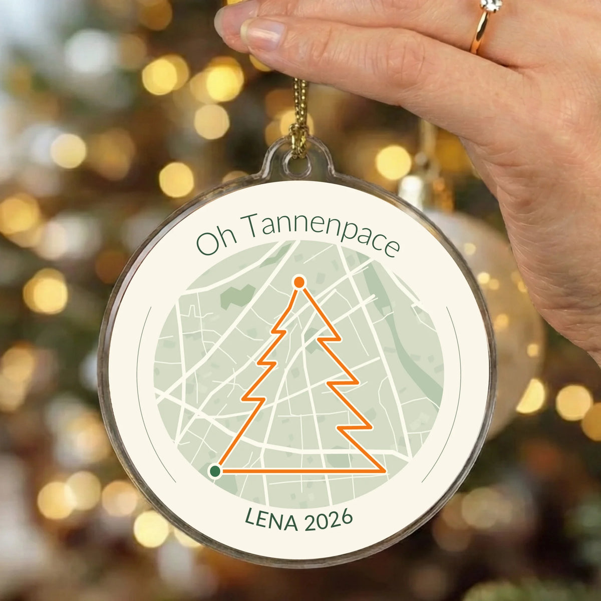 Christbaumschmuck „Oh Tannenpace“ aus Acrylglas mit Goldschnur vor Weihnachtslichtern