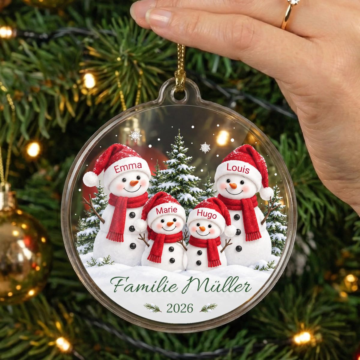Personalisierter Acrylglas-Christbaumschmuck Schneemannfamilie mit vier Namen, Wunschtext und Jahr in der Hand vor einem Weihnachtsbaum